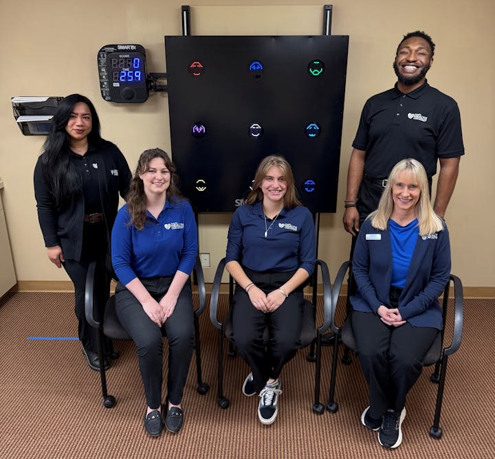 Five people in polo shirts pose together in a clinic or office, with a colorful display board behind them.