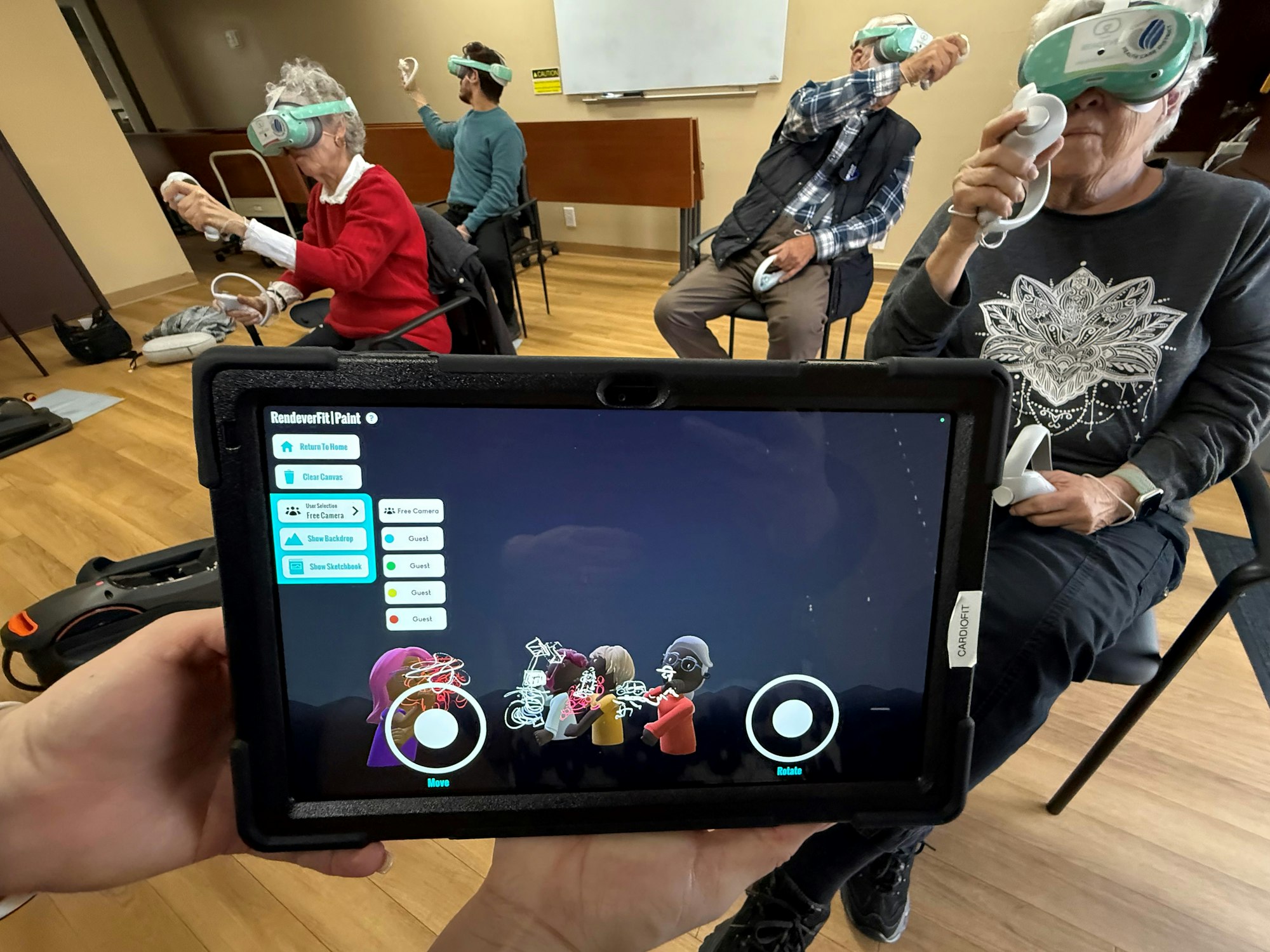 People using VR headsets and controllers in a room, with a tablet displaying a related app.