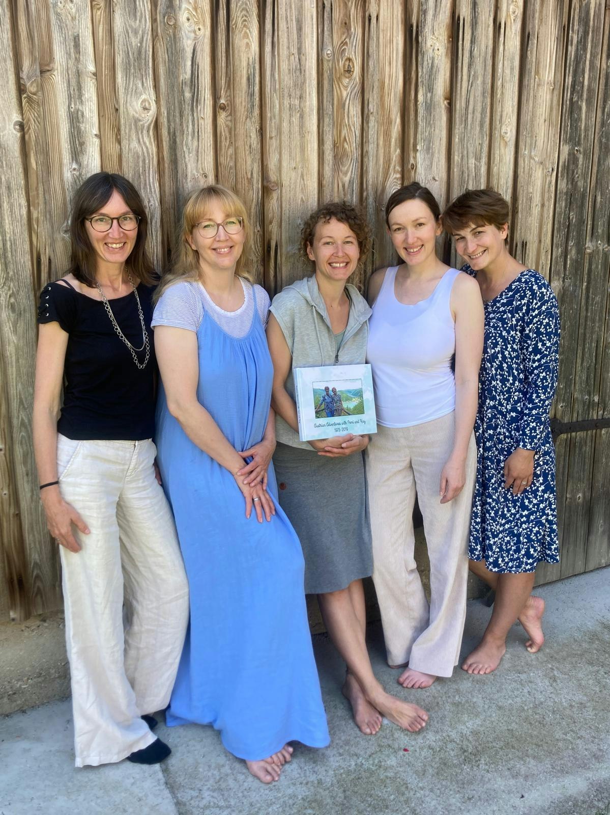 Five smiling people posing in front of a wooden fence, one holding a book.