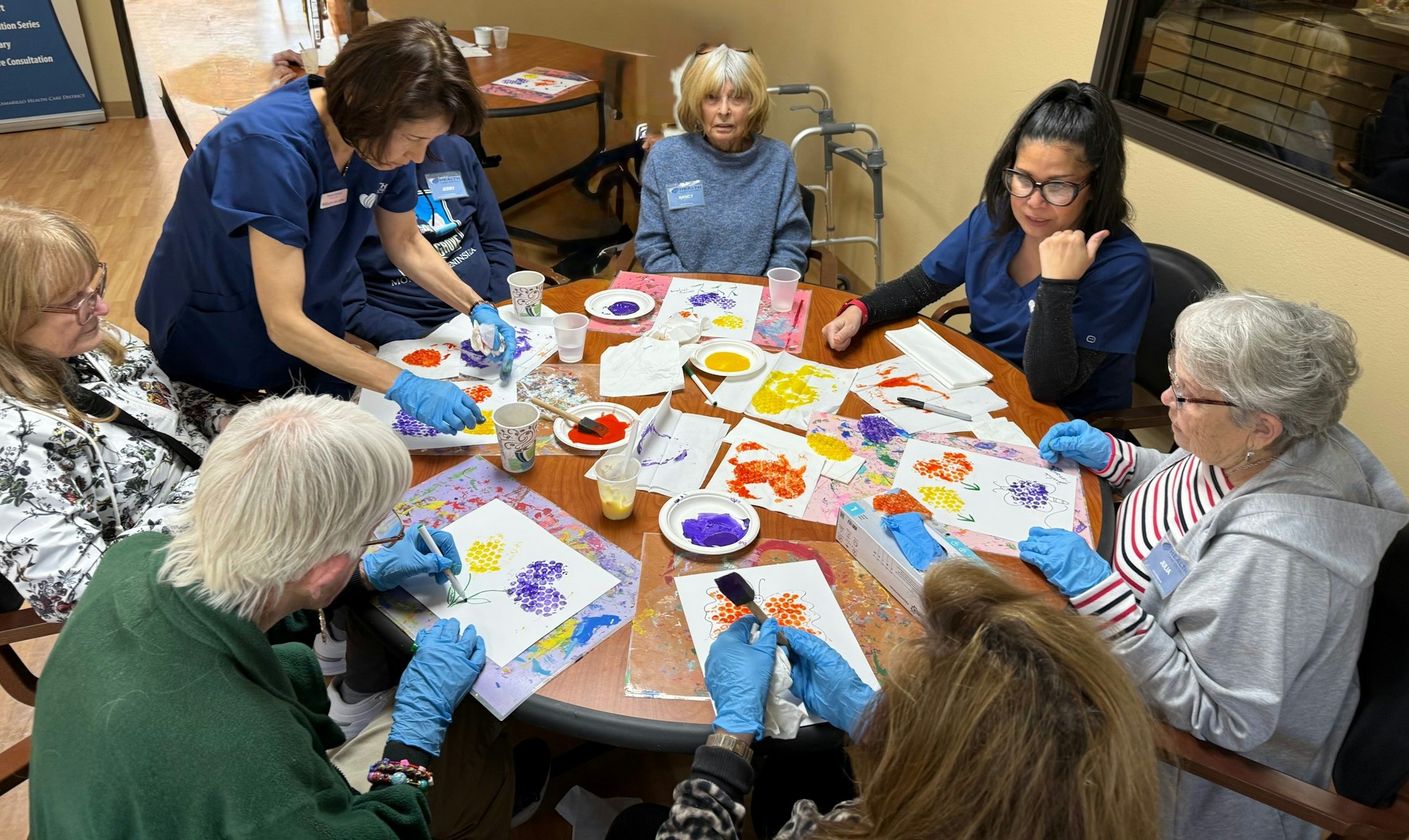 A group of people painting together at a table, with colorful art supplies and canvases in a creative setting.