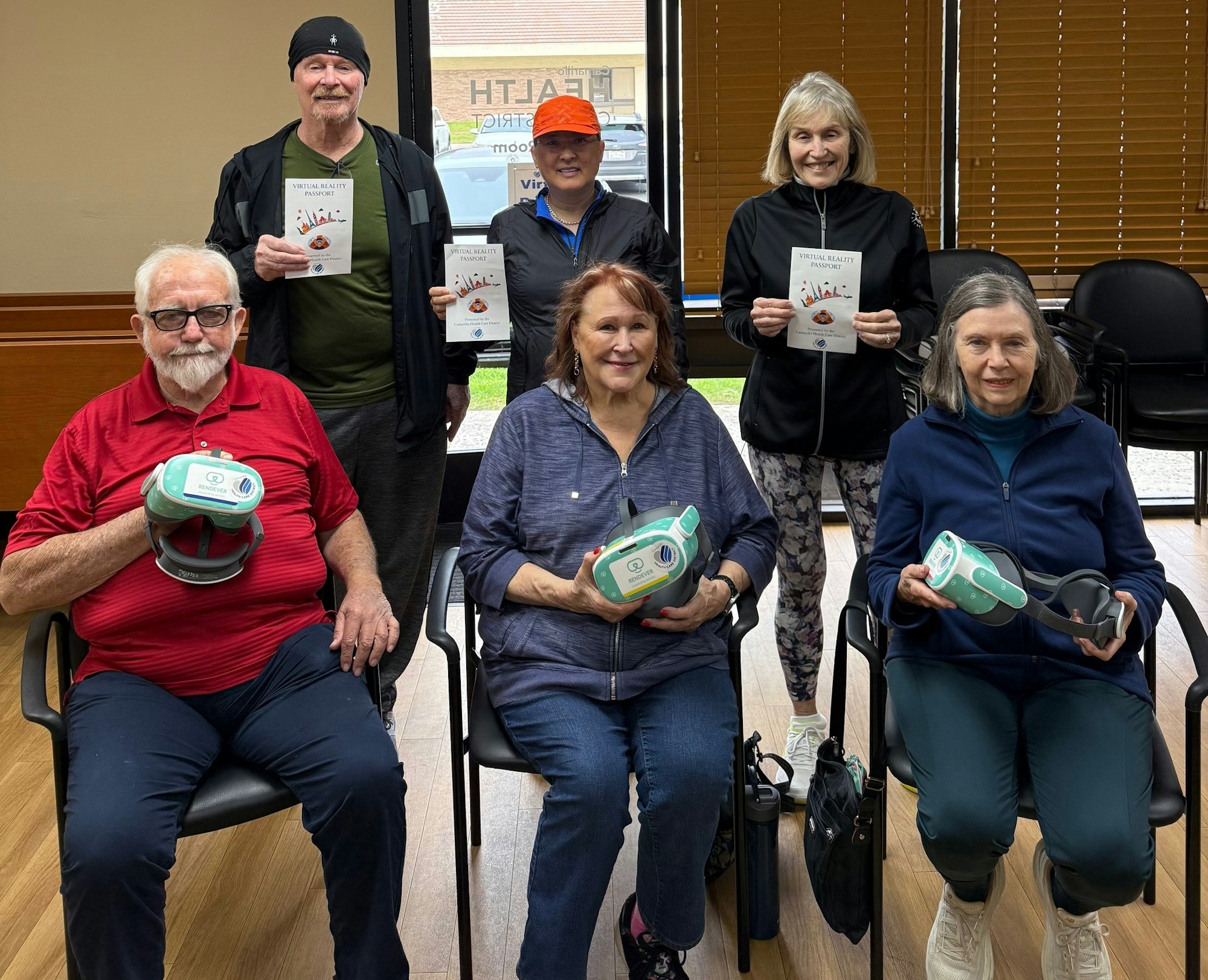 A group of six people sit with VR headsets, holding a 'Virtual Reality Passport' in a community setting.