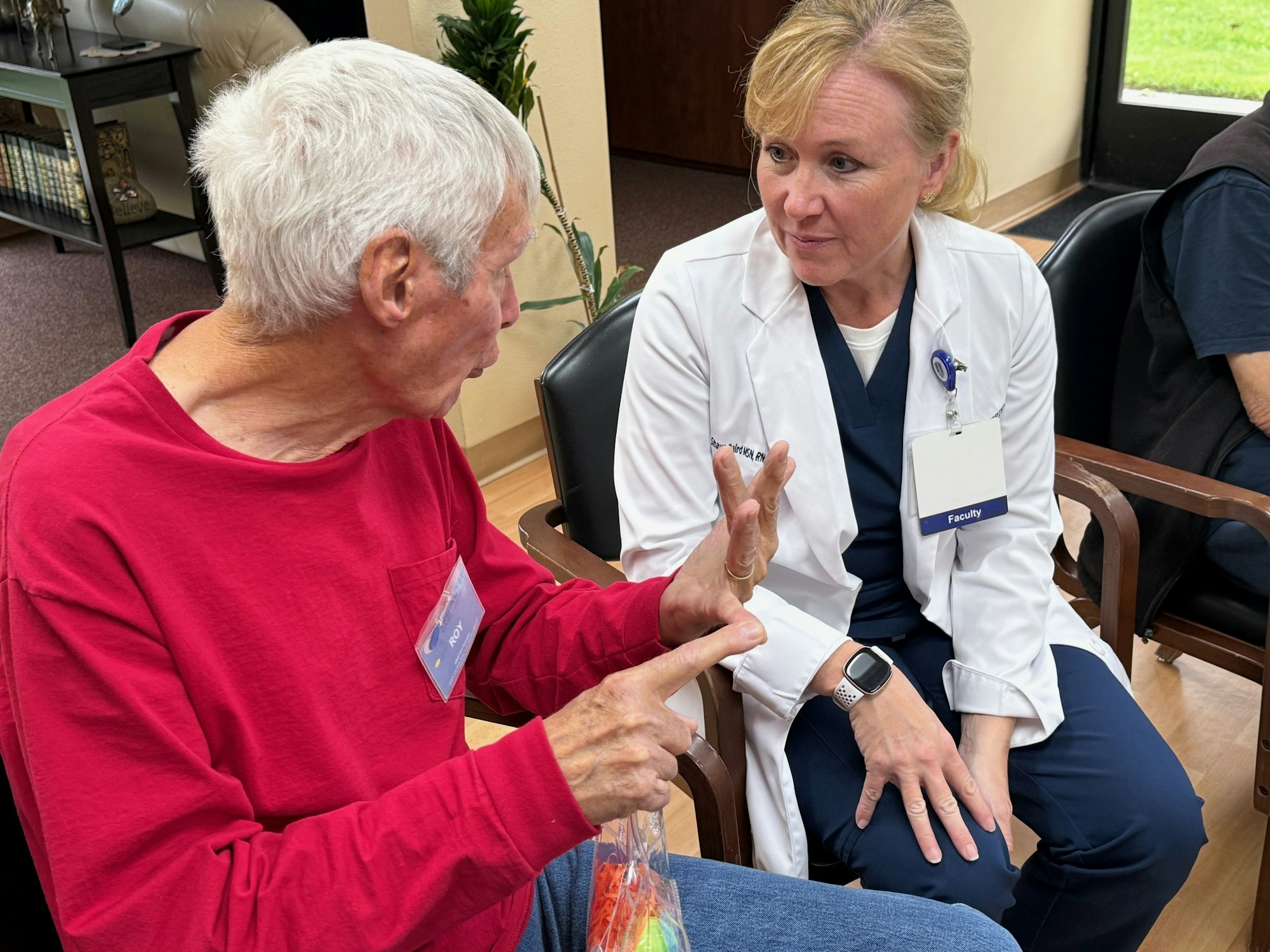 An elderly man in a red shirt is engaged in conversation with a woman in a white coat, likely discussing something important.