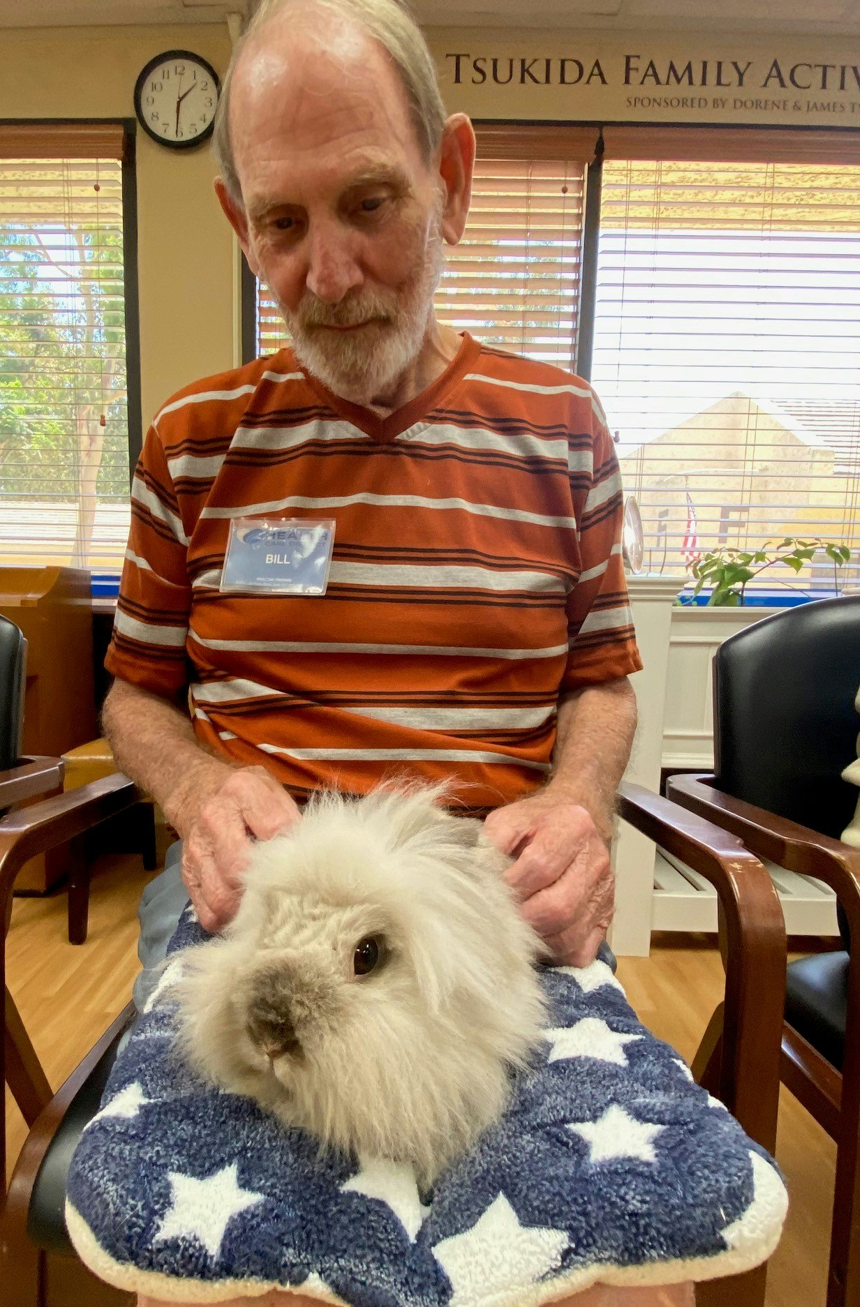 A man with a name tag labeled "BILL" is holding a fluffy rabbit on a star-patterned towel.