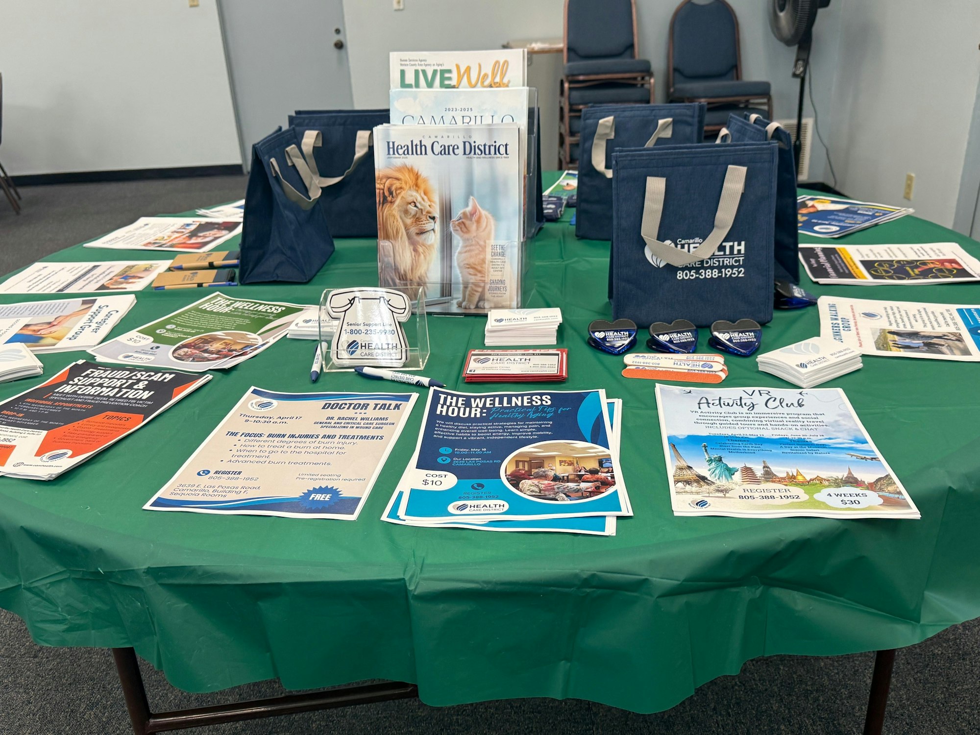A table with pamphlets, brochures, tote bags, and promotional items for a healthcare district event.