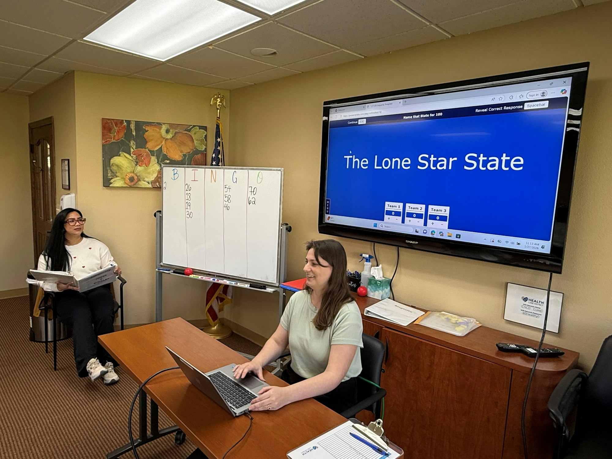 A bingo game in progress with a presentation about Texas, featuring two women and a whiteboard.