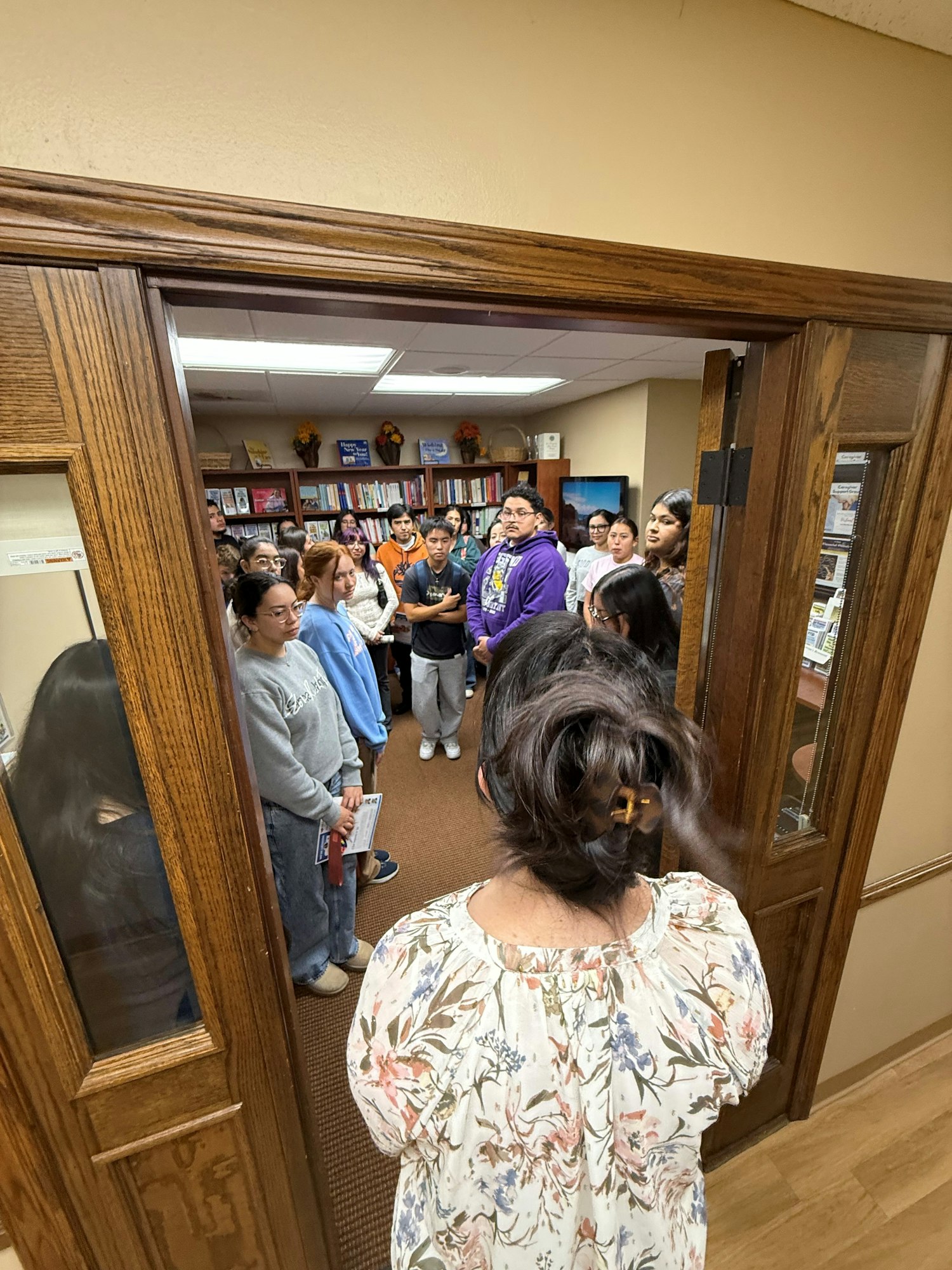 A group of people standing in a room with bookshelves, viewed from a doorway.