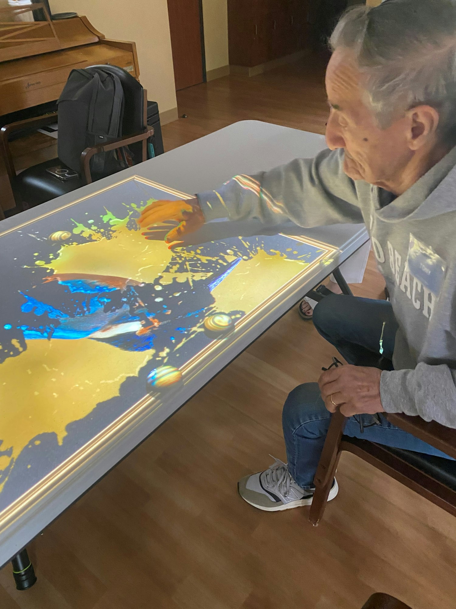 An elderly person is interacting with a colorful digital screen on a table.