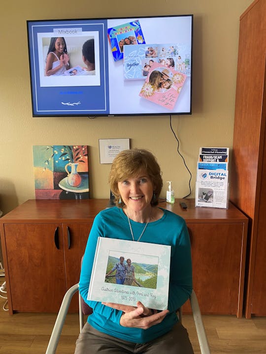 Woman holding a photo book with images of personalized books on the screen behind her.