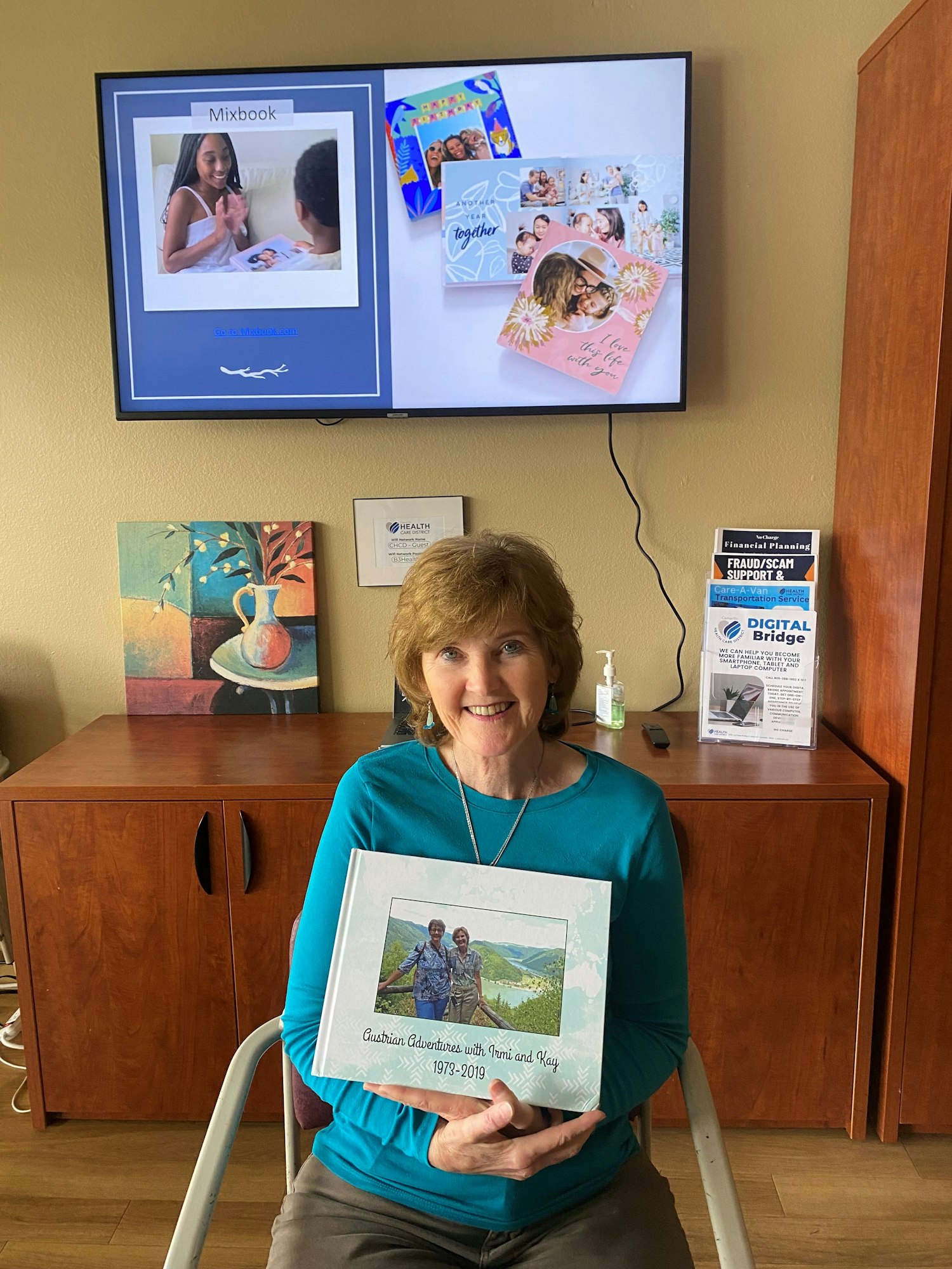 Woman holding a photo book with images of personalized books on the screen behind her.