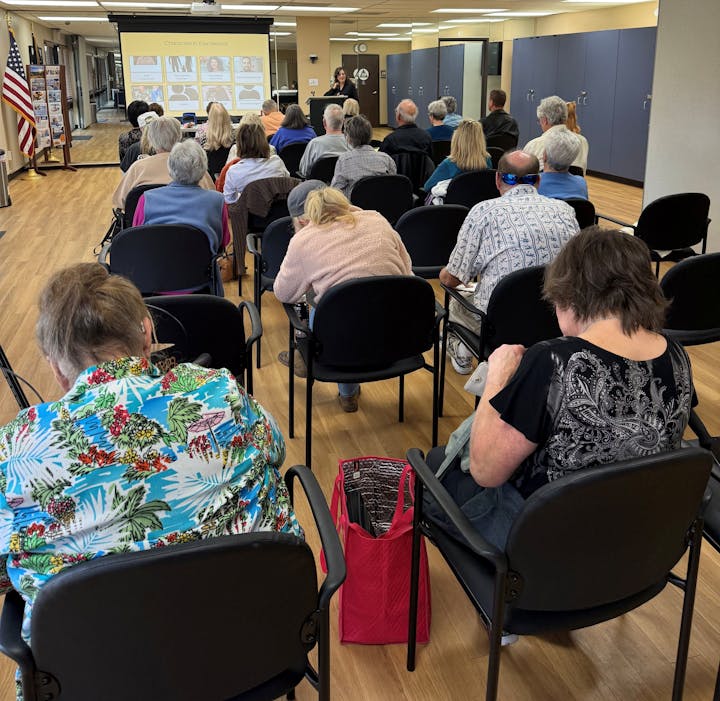 A group of people sitting in chairs, attending a presentation with a speaker at the front and a projector display.