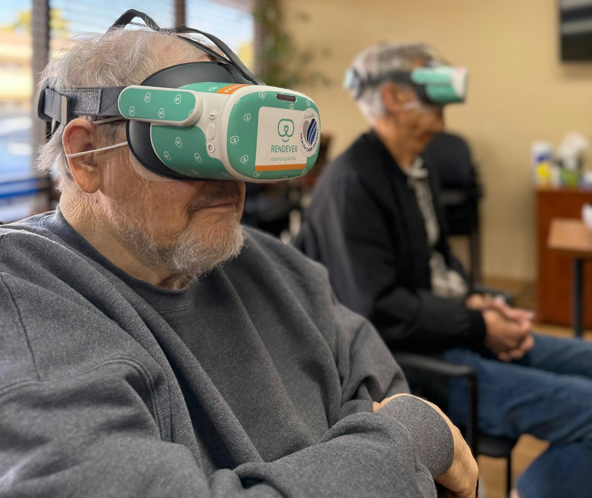 Two people sitting, wearing VR headsets, in an indoor setting.