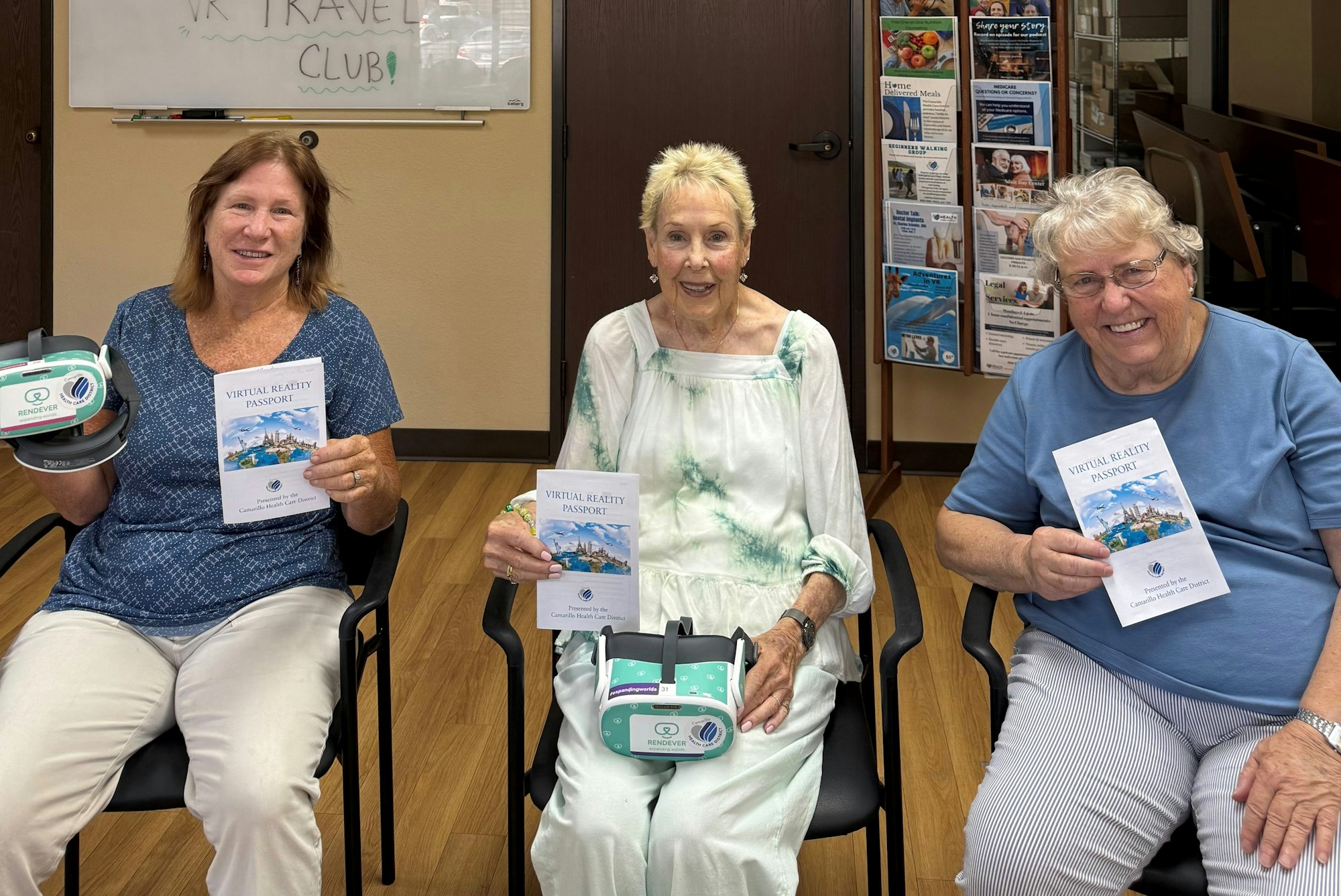 Three people sitting, holding VR headsets and "Virtual Reality Passport" booklets, with a "VR Travel Club" sign in the background.