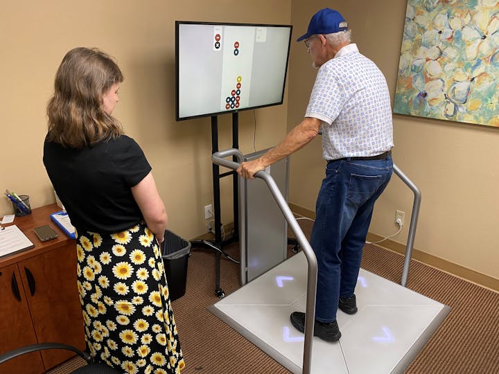 A man on a balance board interacts with a screen while a woman observes in an office setting.