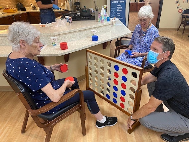 Three people playing a large Connect Four game, with one wearing a mask.