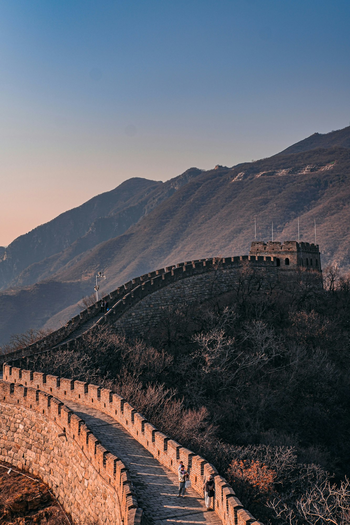 Segment of the Great Wall winding through mountainous terrain with people walking along its path.