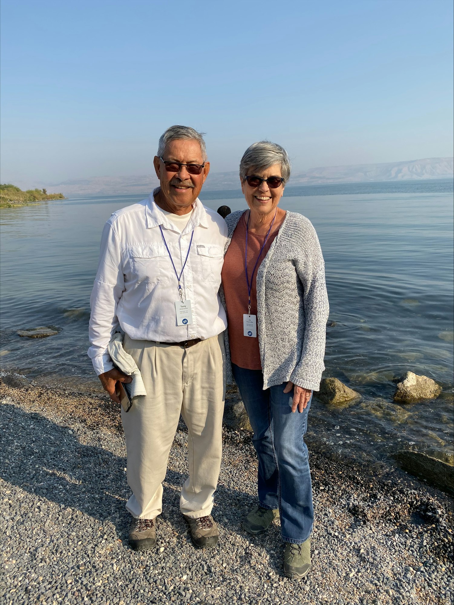 Two smiling people with ID lanyards standing by a calm body of water with mountains in the background.