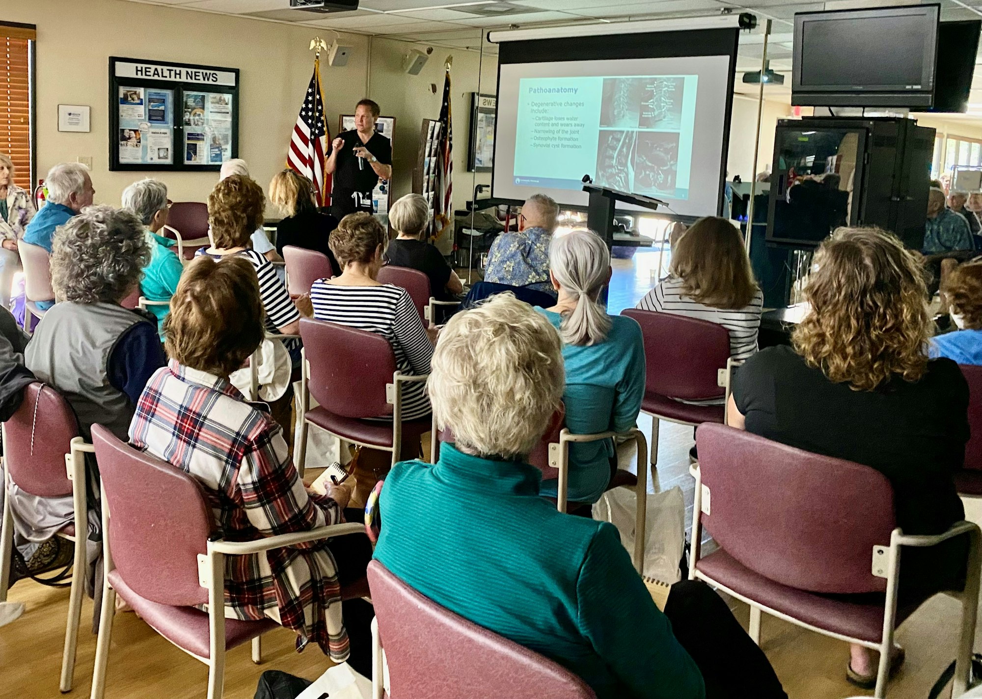 An audience attending a presentation with medical images on the screen, indicating a health-related lecture or seminar.