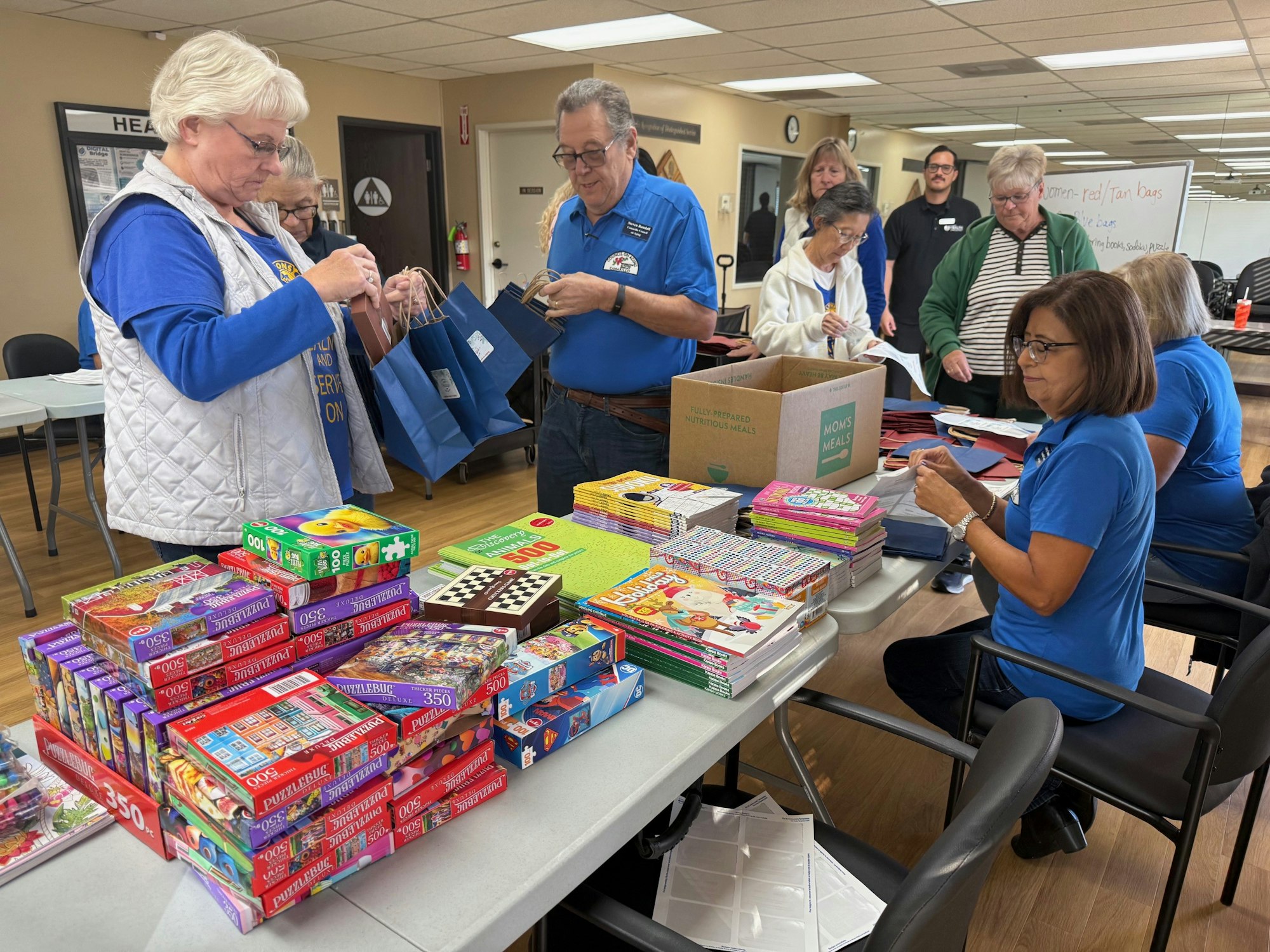 Group of people assembling care packages with puzzles and books at a table.