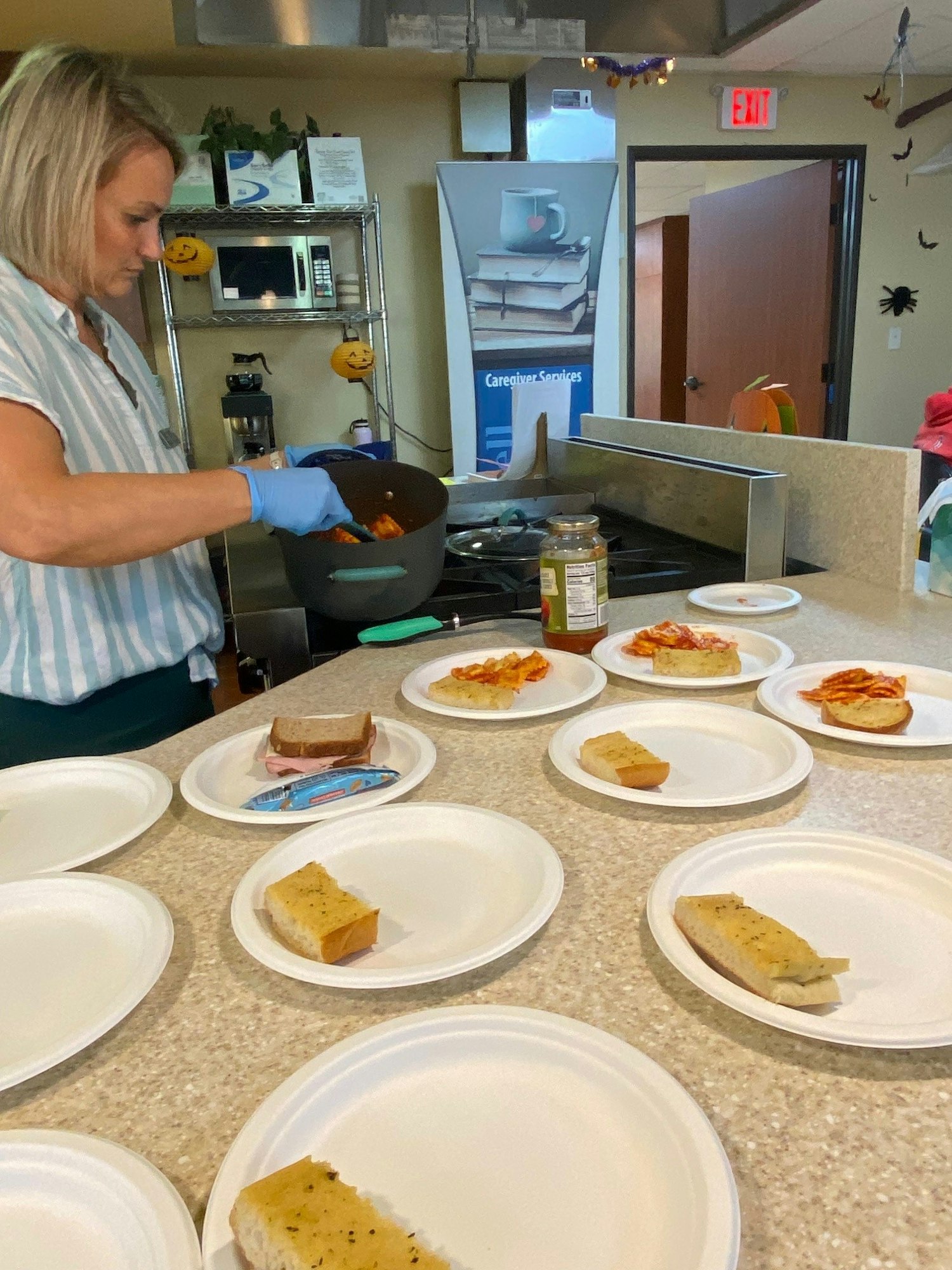 Person serving food on multiple plates, kitchen counter, possibly a communal dining setting.