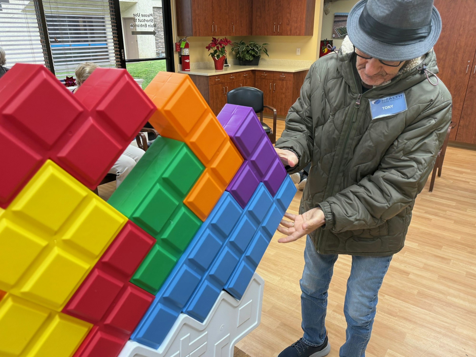 A person in a jacket and hat interacts with large colorful blocks in a room with wooden floors.