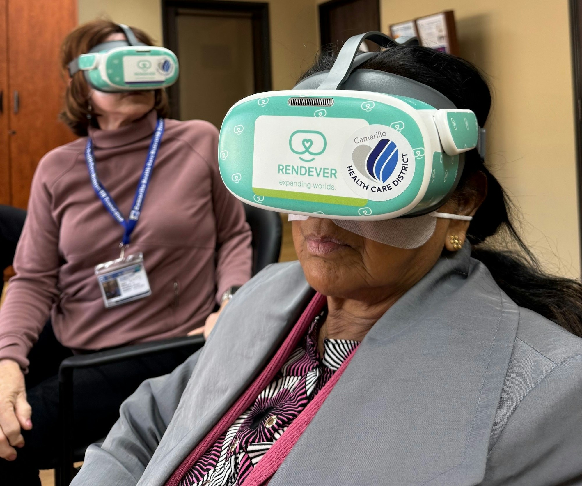 Two people wearing VR headsets branded with "Rendever" and "Camarillo Health Care District" in an indoor setting.