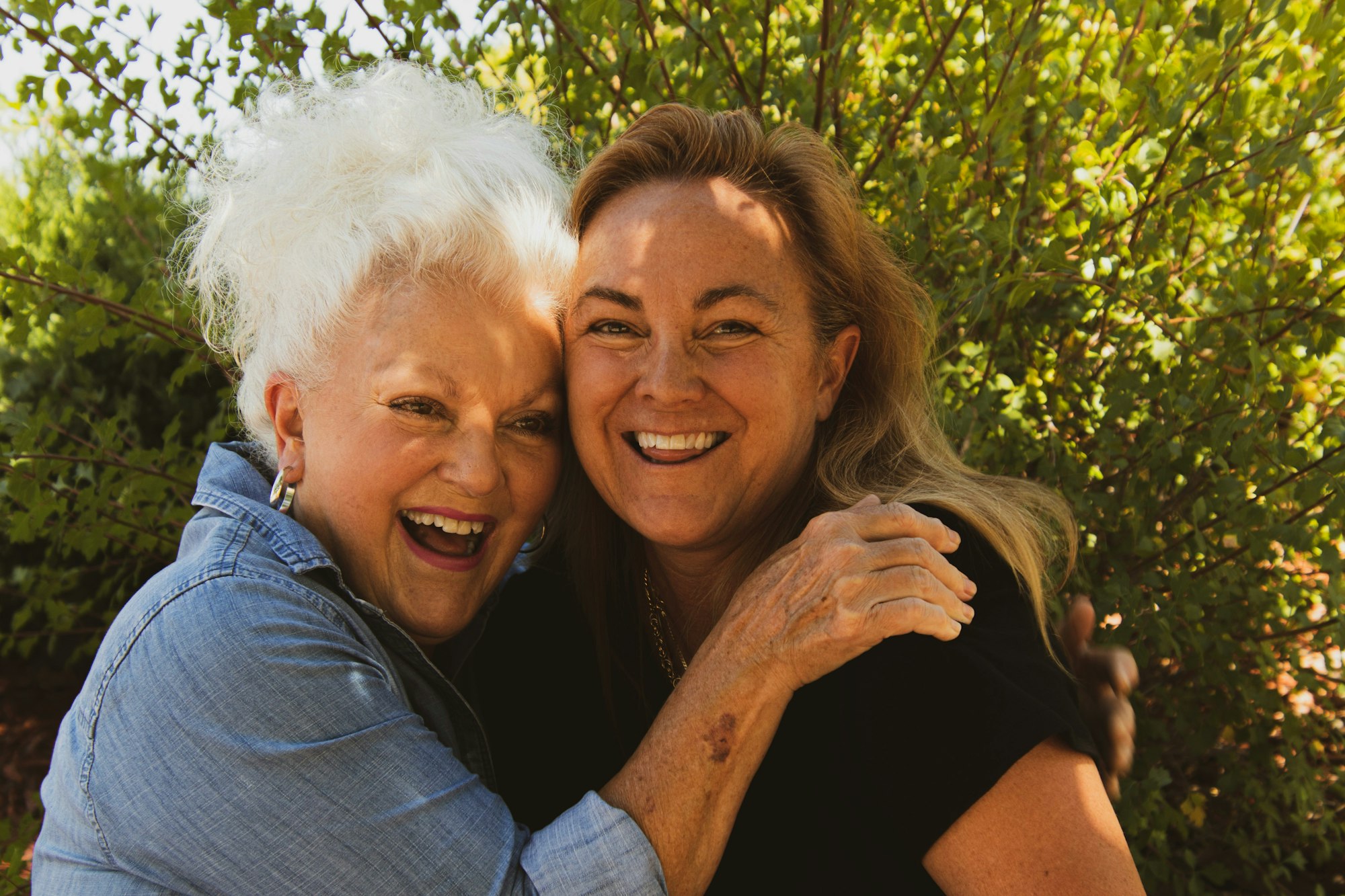 Two women hugging and smiling outdoors.
