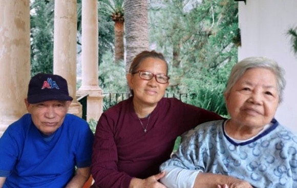 A group of three people sitting together in a lush outdoor setting, smiling and enjoying each other's company.