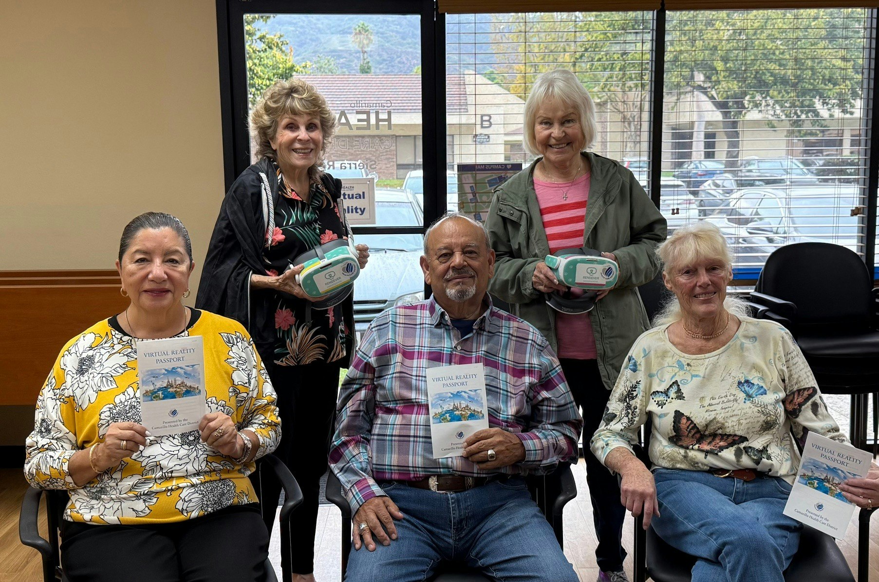 Five people holding virtual reality headsets and brochures in a room, smiling at the camera.