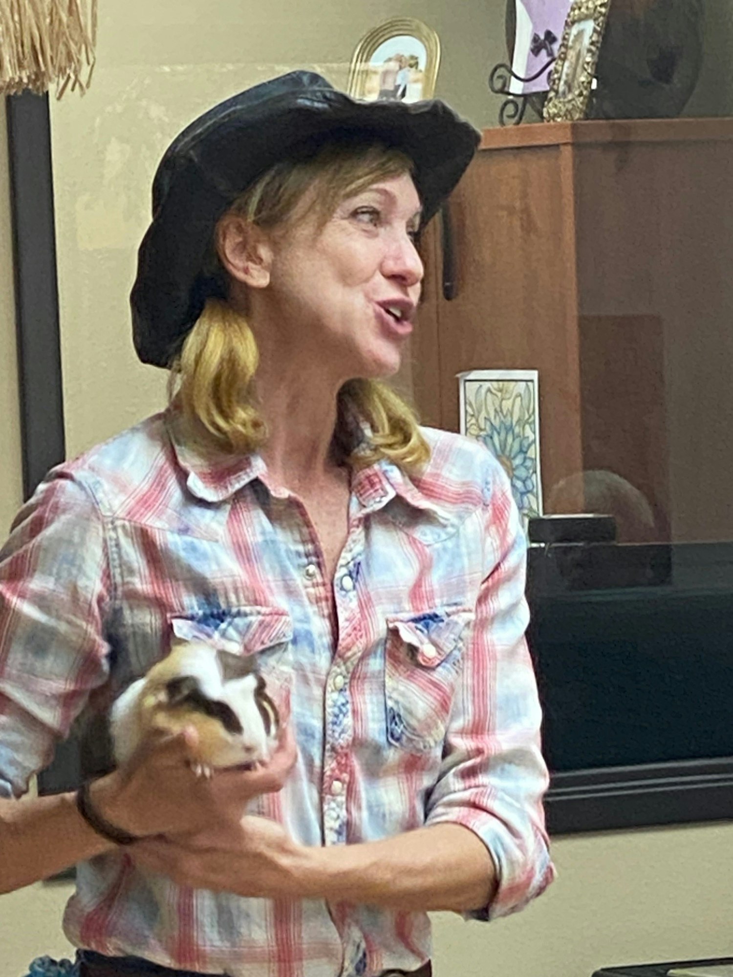 A woman in a plaid shirt and black hat holding a guinea pig.