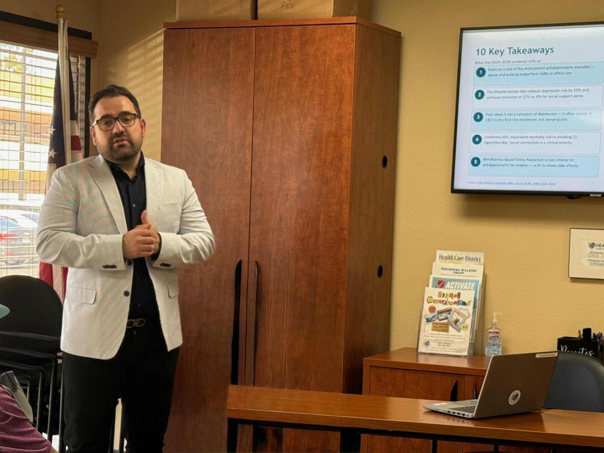 A person presents key takeaways on health and wellness topics in a meeting room, with a screen displaying information behind them.