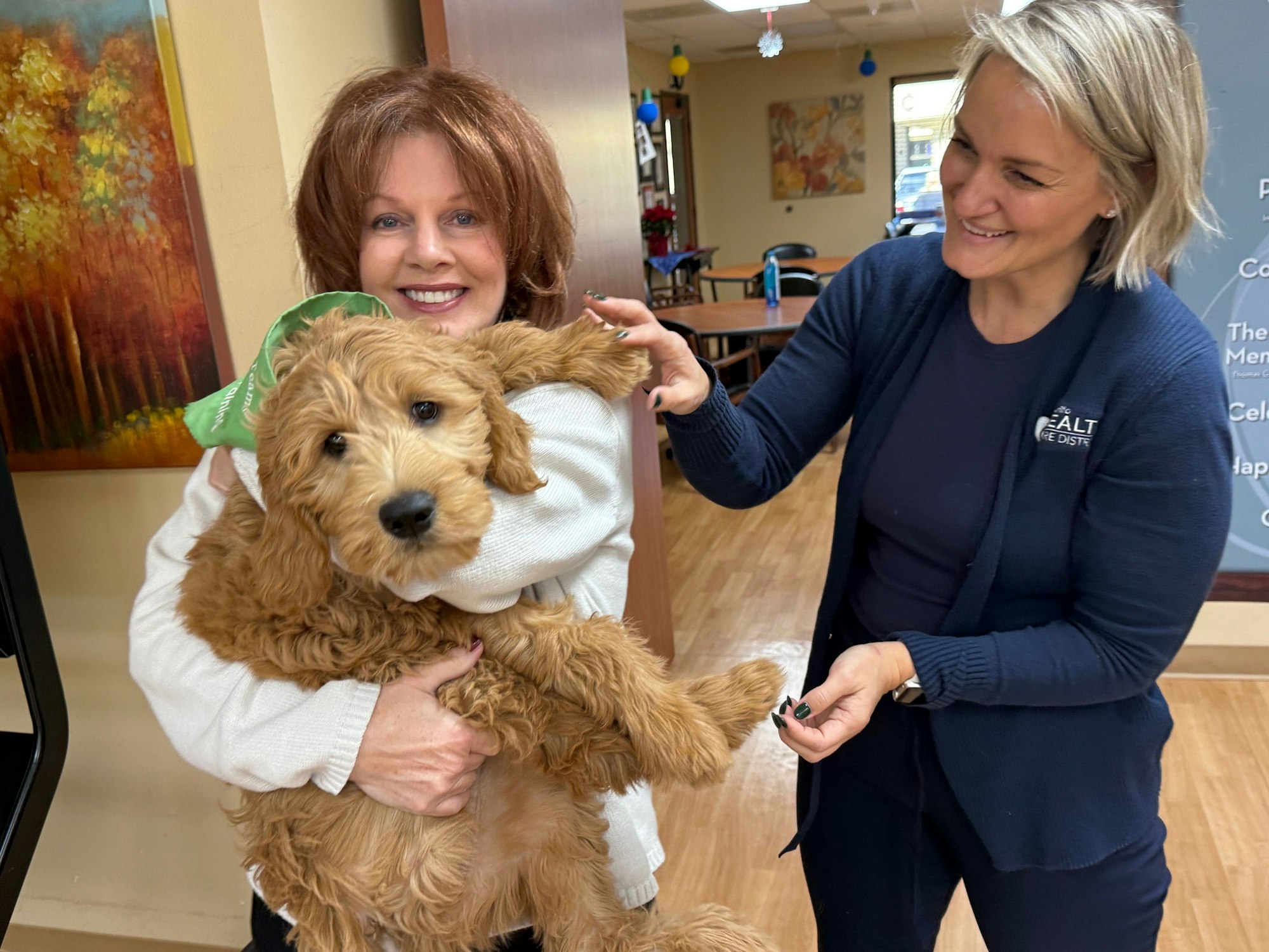 Two people smile while holding a fluffy brown dog.