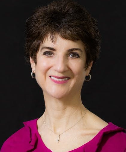A portrait of a smiling woman with short hair, wearing earrings, a fuchsia top, and a necklace against a black background.