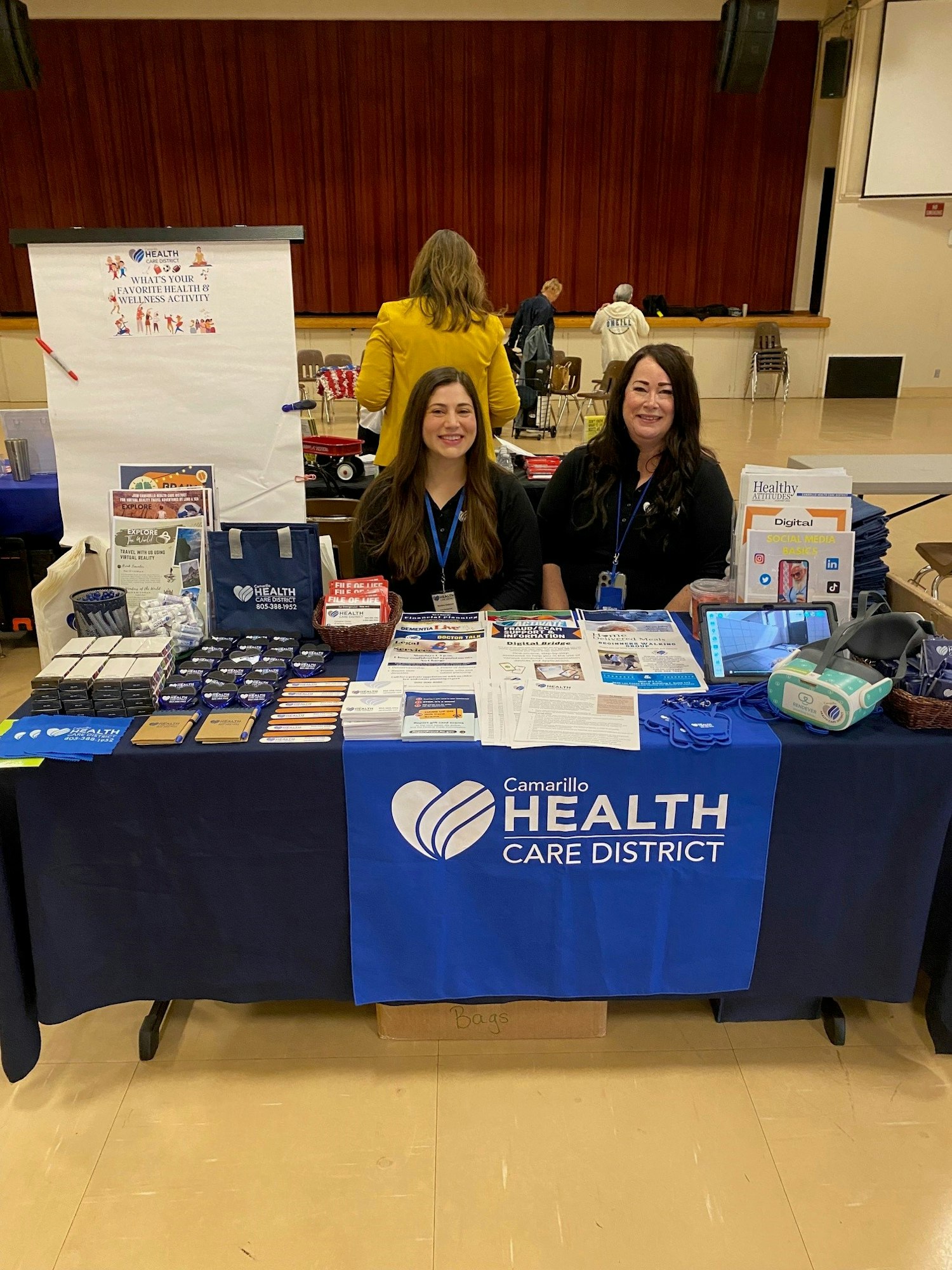 Two individuals at a "Camarillo Health Care District" informational booth with educational materials and promotional items.