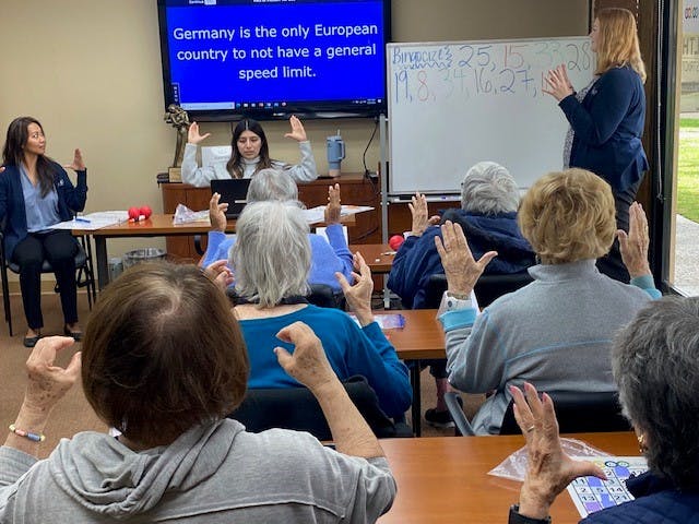 Classroom of students and three instructors with their hands in the air playing Bingocize.