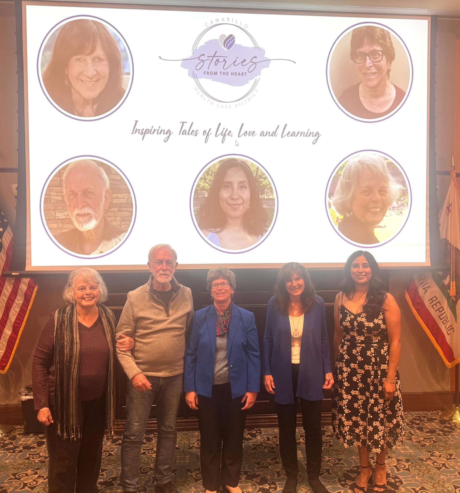 A group of six people stand in front of a screen featuring portraits and the text "Stories from the Heart: Inspiring Tales of Life, Love and Learning."
