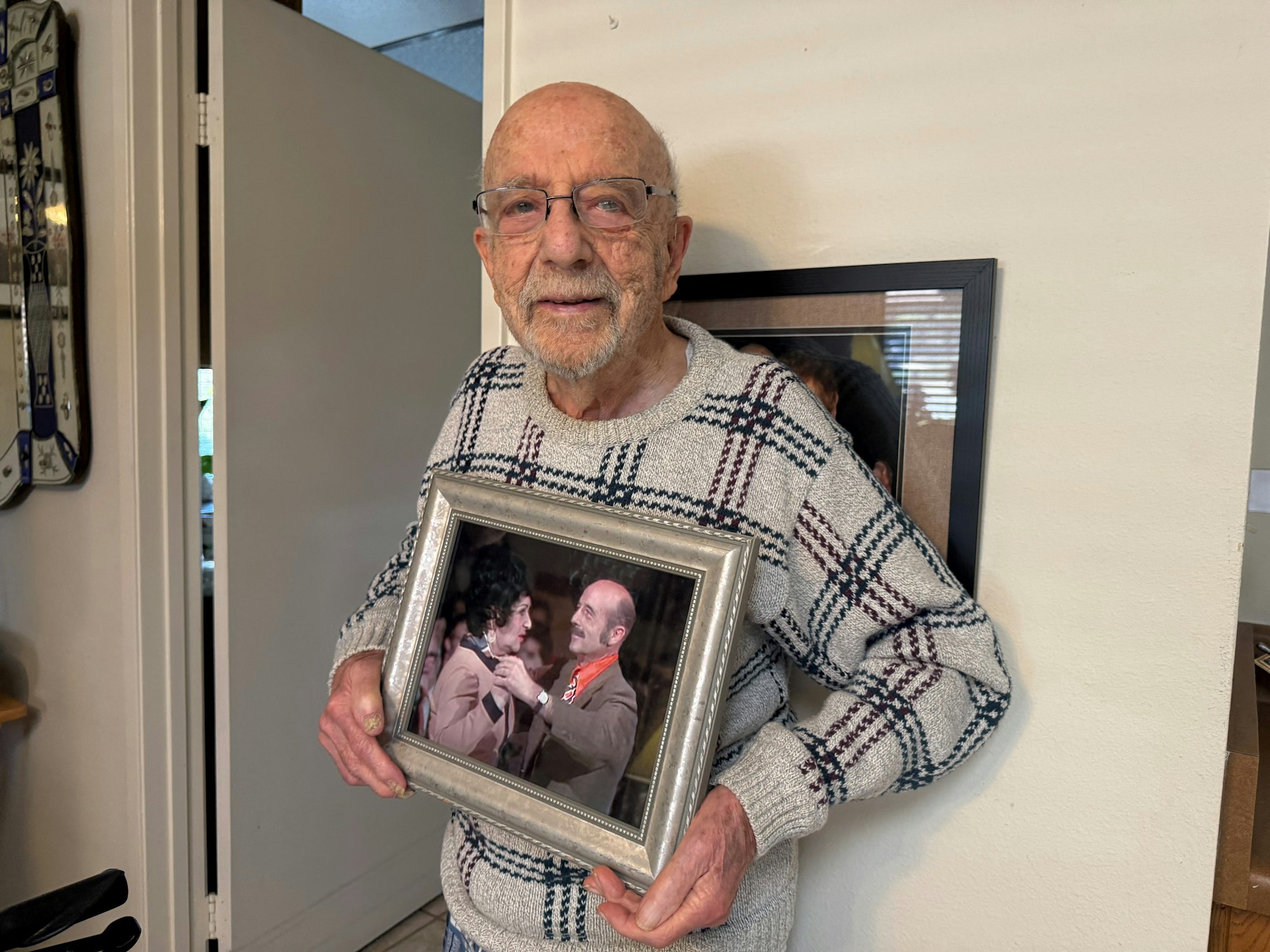 An elderly person holds a framed photograph of two people in a happy moment.
