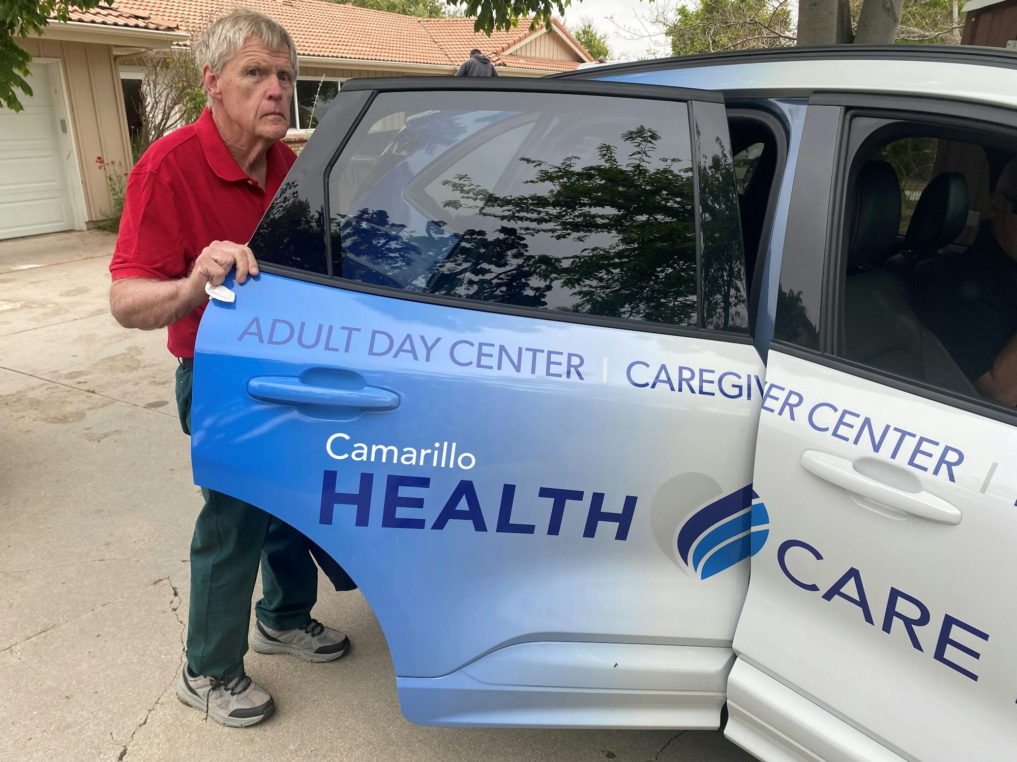 A man is applying a decal to a vehicle that advertises a health care facility.