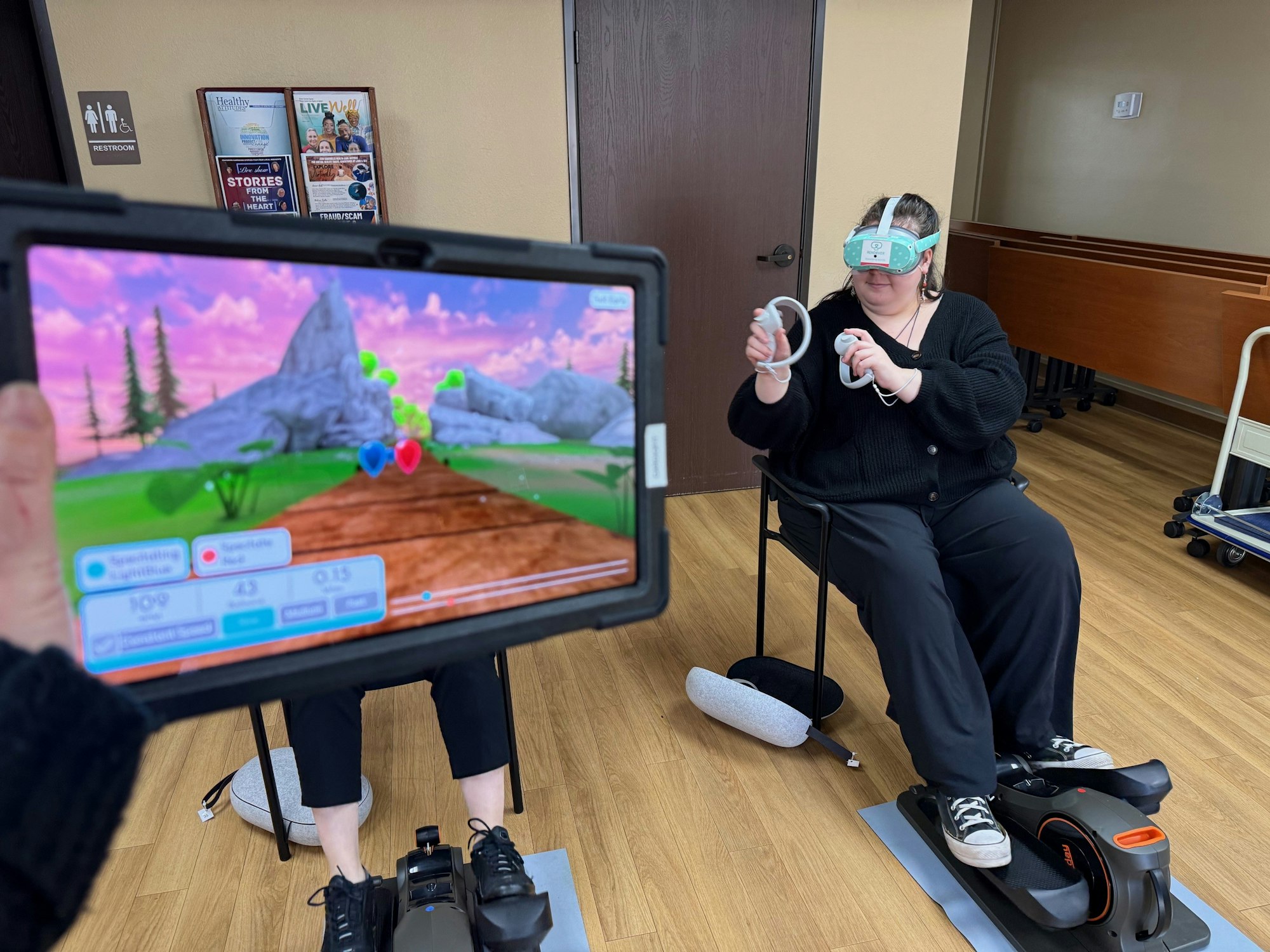 Person using VR and exercise equipment, tablet in foreground displaying a game interface.