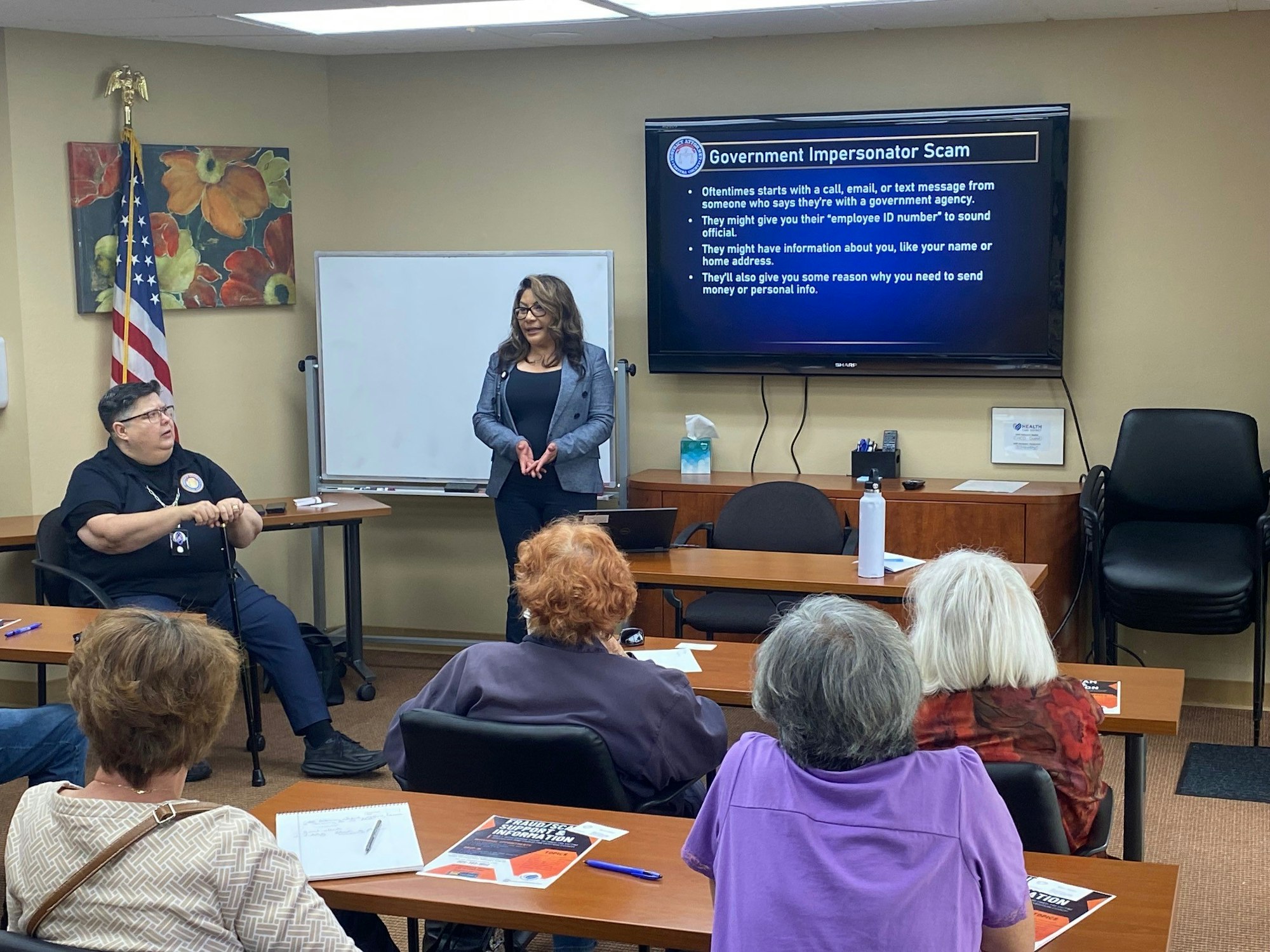 A presentation about Government Impersonator Scams, with two speakers and an audience in a room.