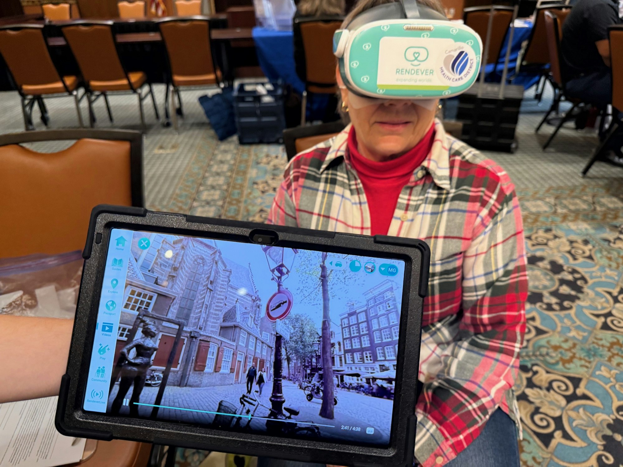 A person wearing a VR headset labeled "Rendever," with a tablet showing a cityscape image.