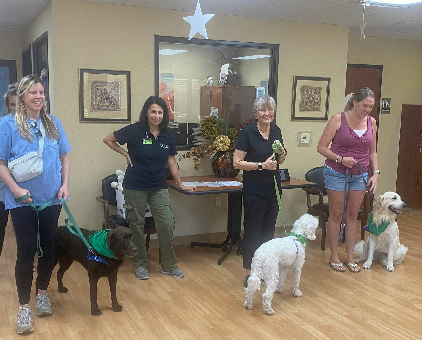 Four people and three dogs in a room, possibly at a vet or pet event. Everyone seems happy and relaxed.