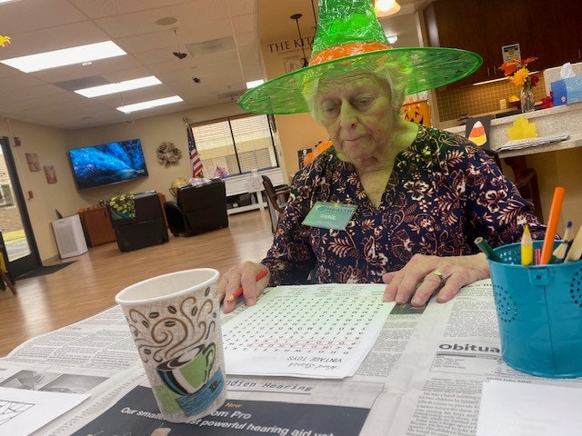 May contain: woman, adult, female, person, hat, clothing, pen, table, furniture, portrait, photography, head, face, chair, desk, reading, disposable cup, cup, text, monitor, screen, hardware, electronics, and computer hardware