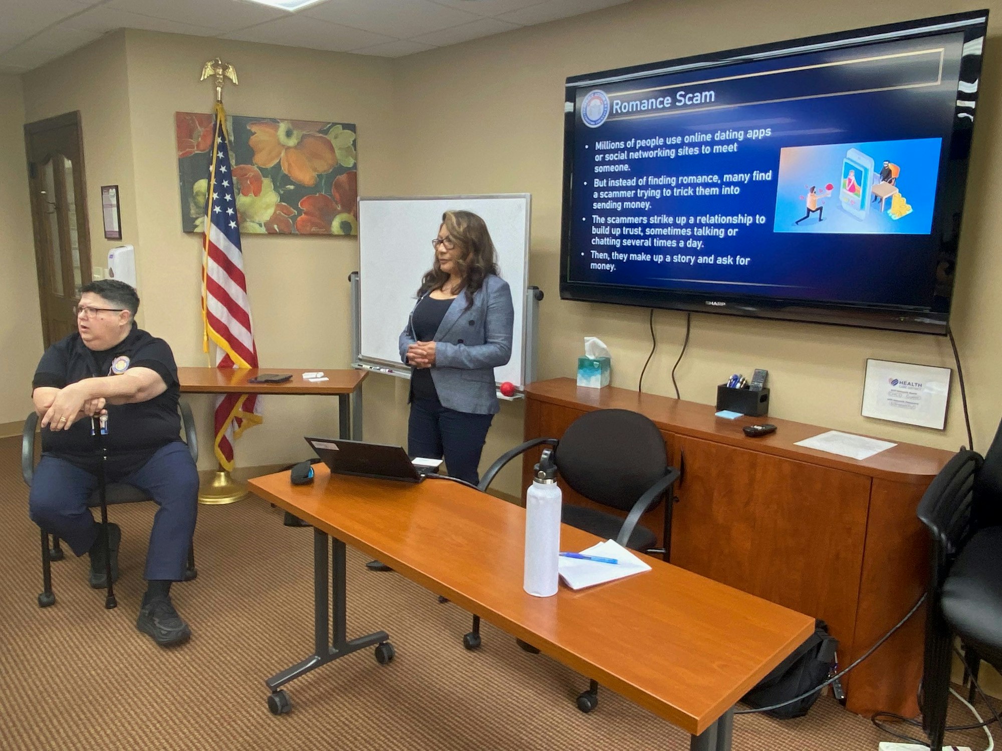 Two people in a room with a presentation about romance scams on a screen.