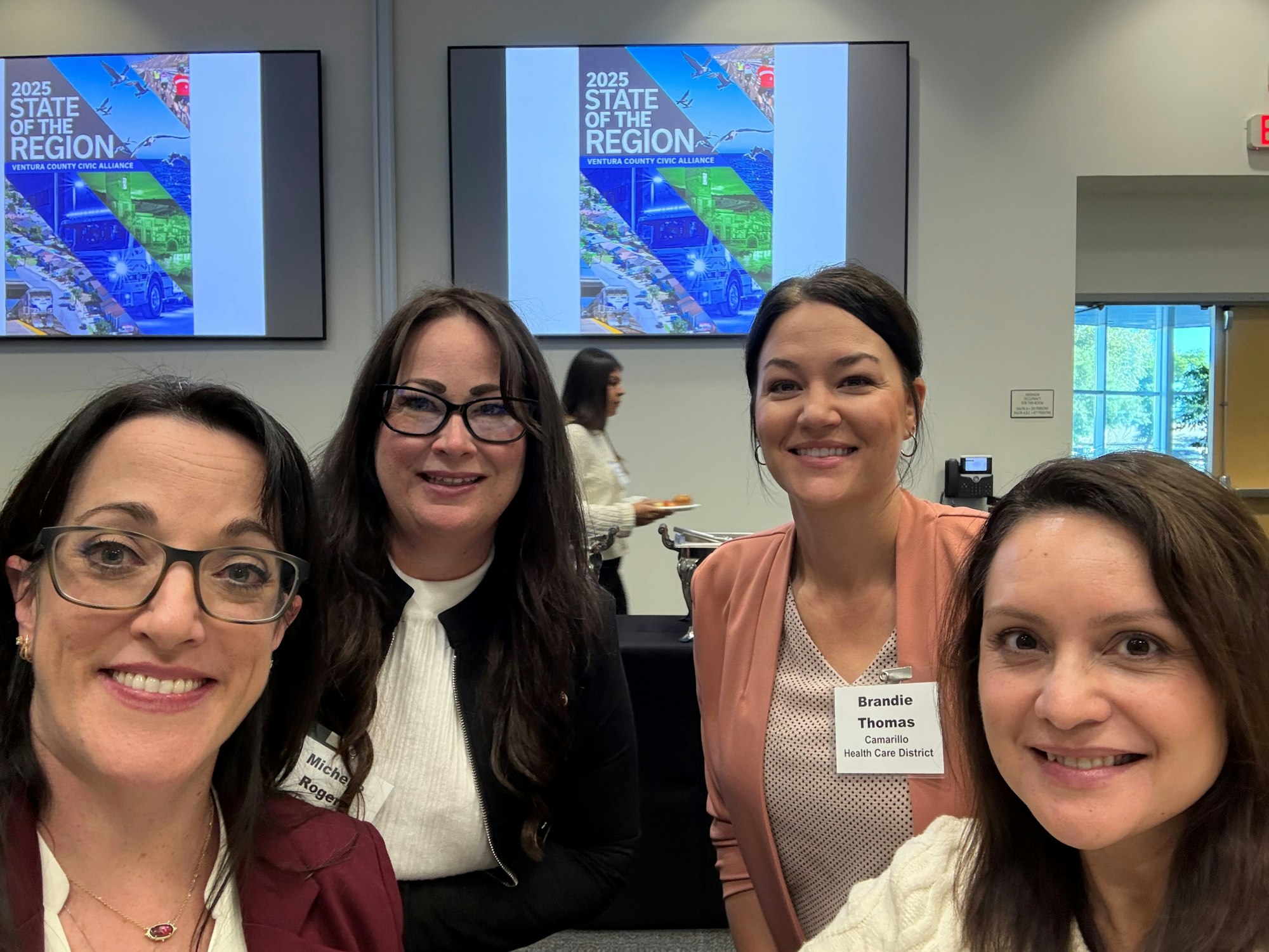 Four women smiling at a "2025 State of the Region" event with name tags.