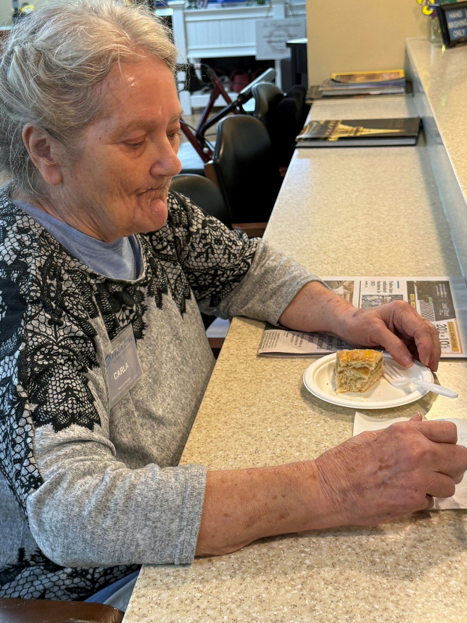 A person sitting at a counter with a slice of cake on a plate, reading a newspaper.