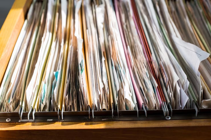 A wooden filing cabinet drawer filled with neatly organized folders and documents, showcasing various colors and paper types.