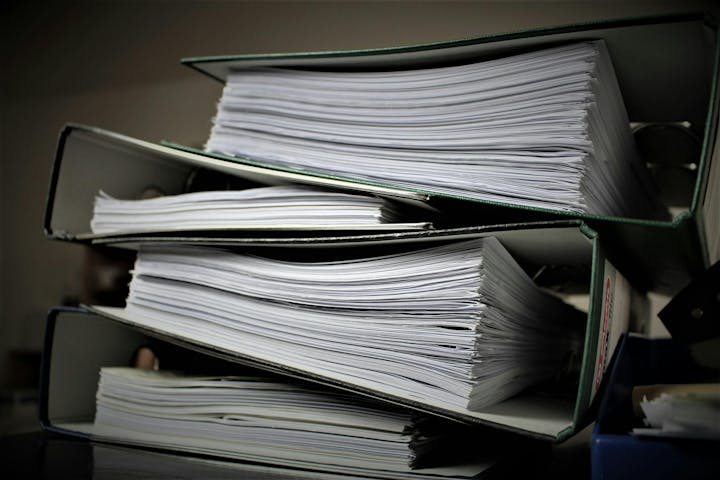 The image shows several stacked binders filled with sheets of paper, suggesting organized documents or reports.