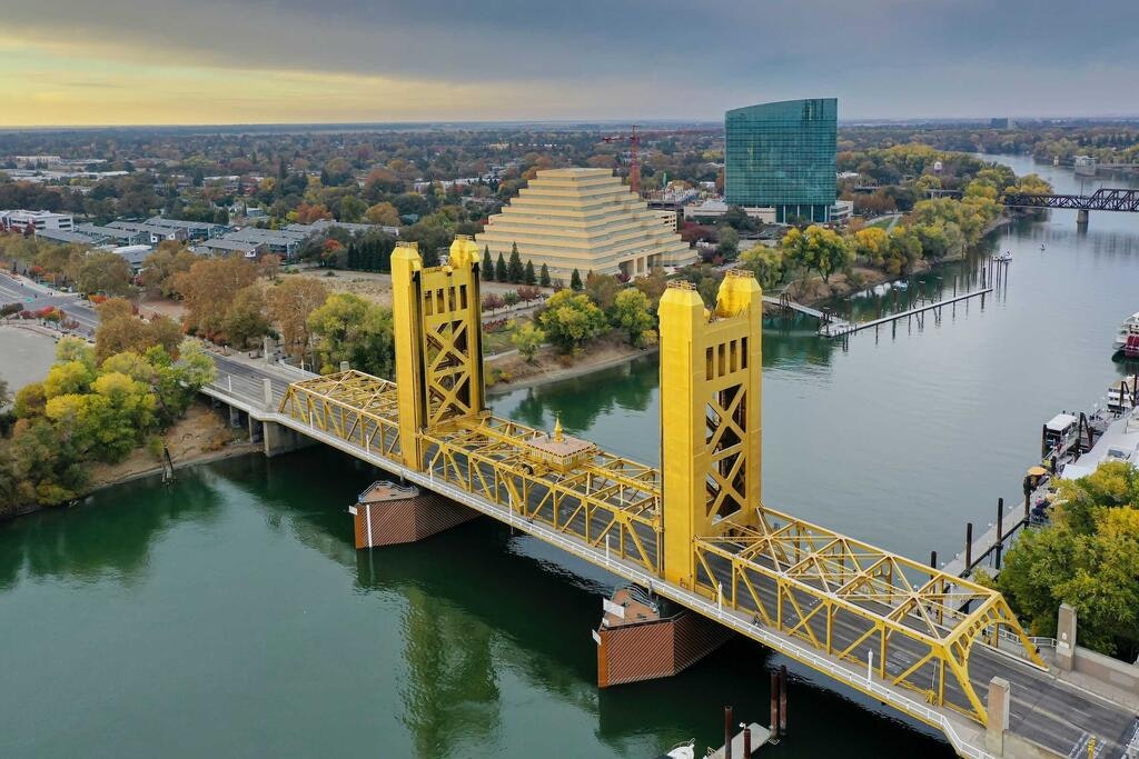 Aerial view of a yellow lift bridge over a river with cityscape and autumn trees.