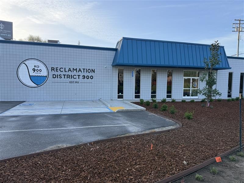 The image shows a modern building for Reclamation District 900, established in 1911, with landscaping and a blue roof.
