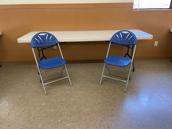 A simple room setup featuring a long table and two blue folding chairs.